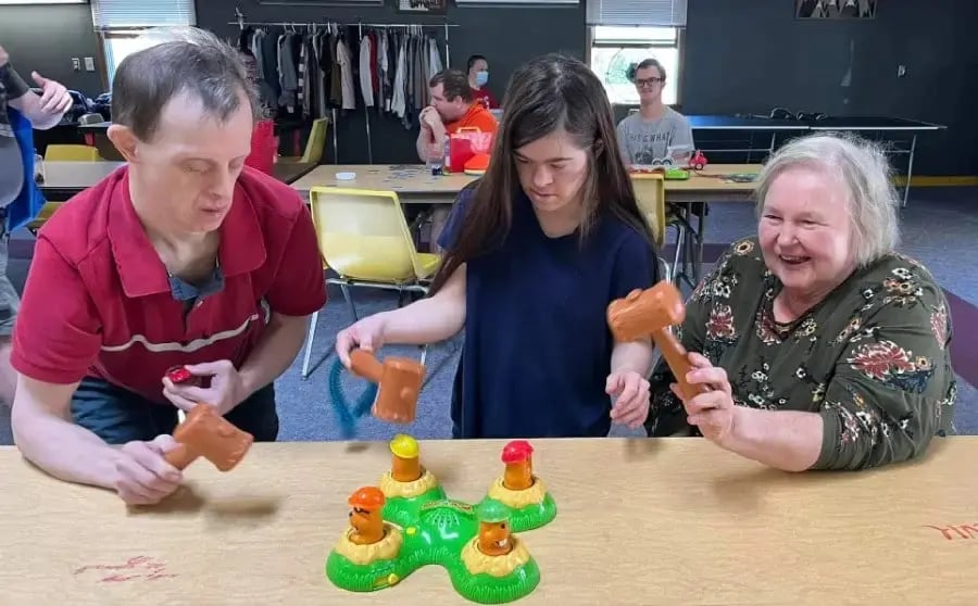 Adults playing a whack-a-mole game in a vocational day program group activity.